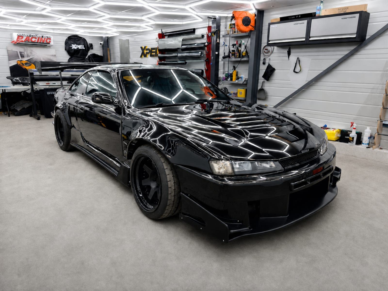 Nissan Silvia S14 noire body kit large vue trois-quarts avant dans l'atelier AWD sous l'éclairage hexagonal, après pose XPEL Ultimate sur-mesure